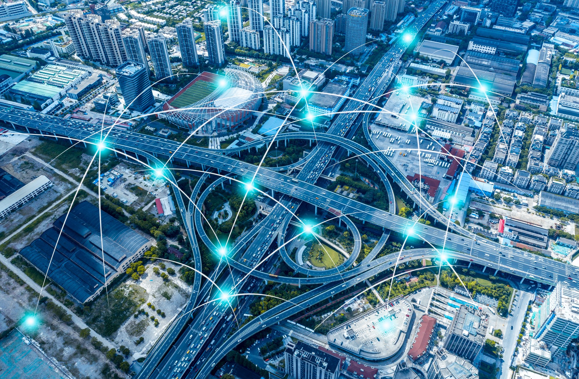 Aerial view of a complex urban highway system overlaid with glowing blue digital networks, symbolizing Cox 2M's IoT solutions that enhance business connectivity and efficiency across.