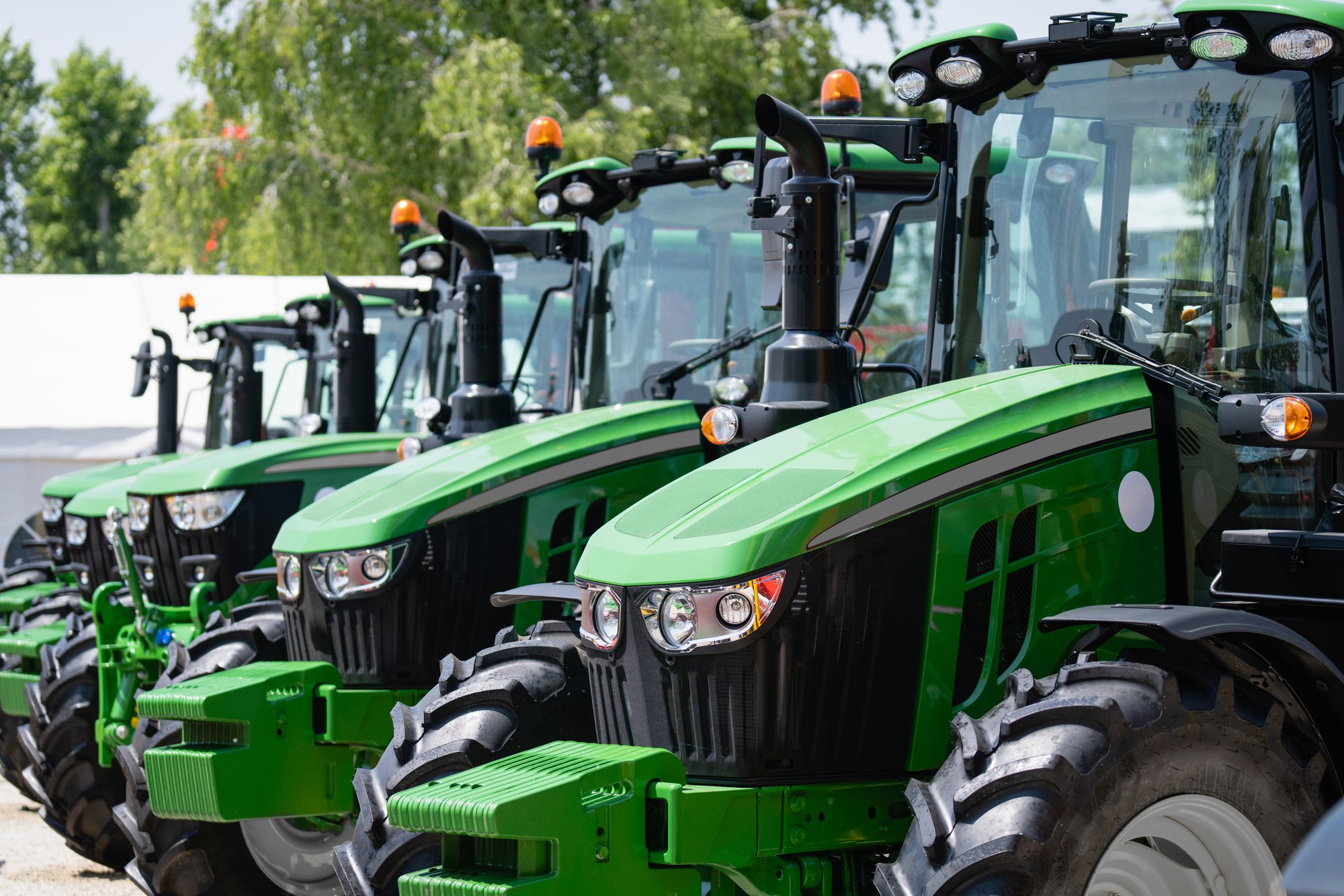 Row of advanced green tractors equipped with monitoring and safety features, lined up and ready for use. Each tractor showcases the integration of asset protection and monitoring technology, ideal for securing valuable agricultural equipment.
